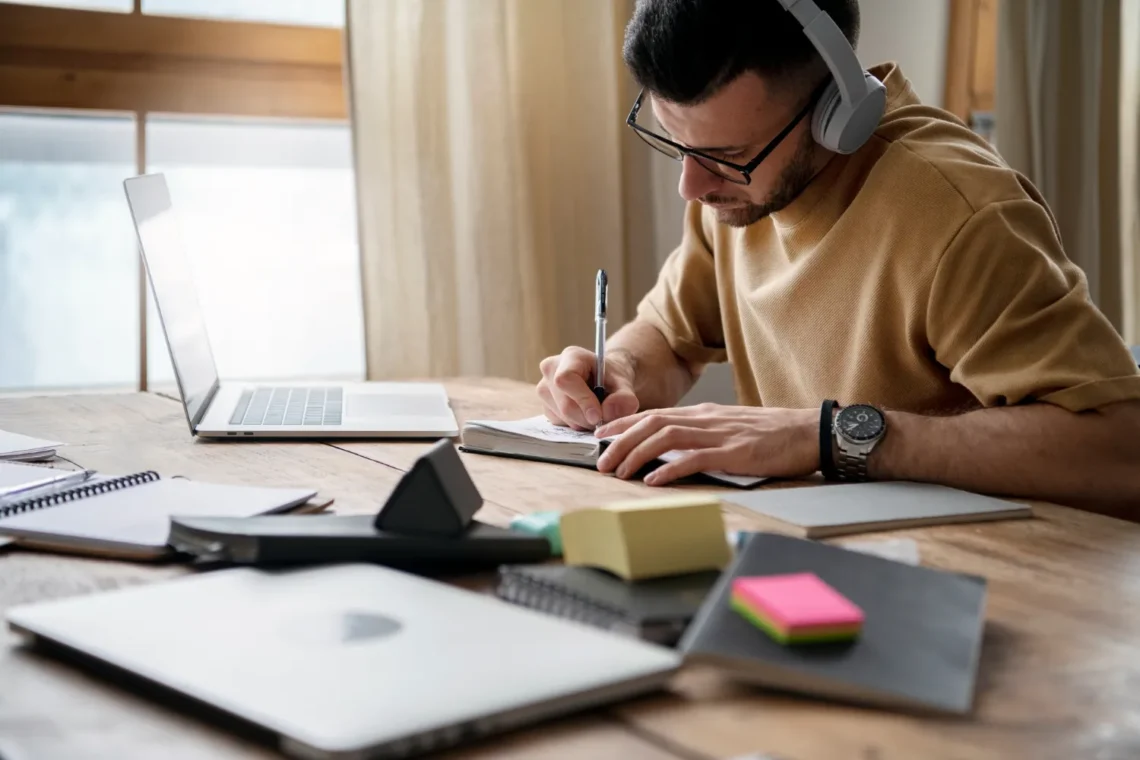 Preparação para o Concurso Seplan SE – Foco nos Estudos! Homem estudando em uma mesa com fones de ouvido e anotações ao lado do laptop