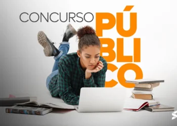 Jovem estudando para concurso público com laptop e livros ao redor.
