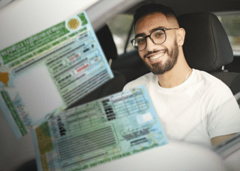 Jovem sorridente exibindo a CNH gratuita dentro do carro