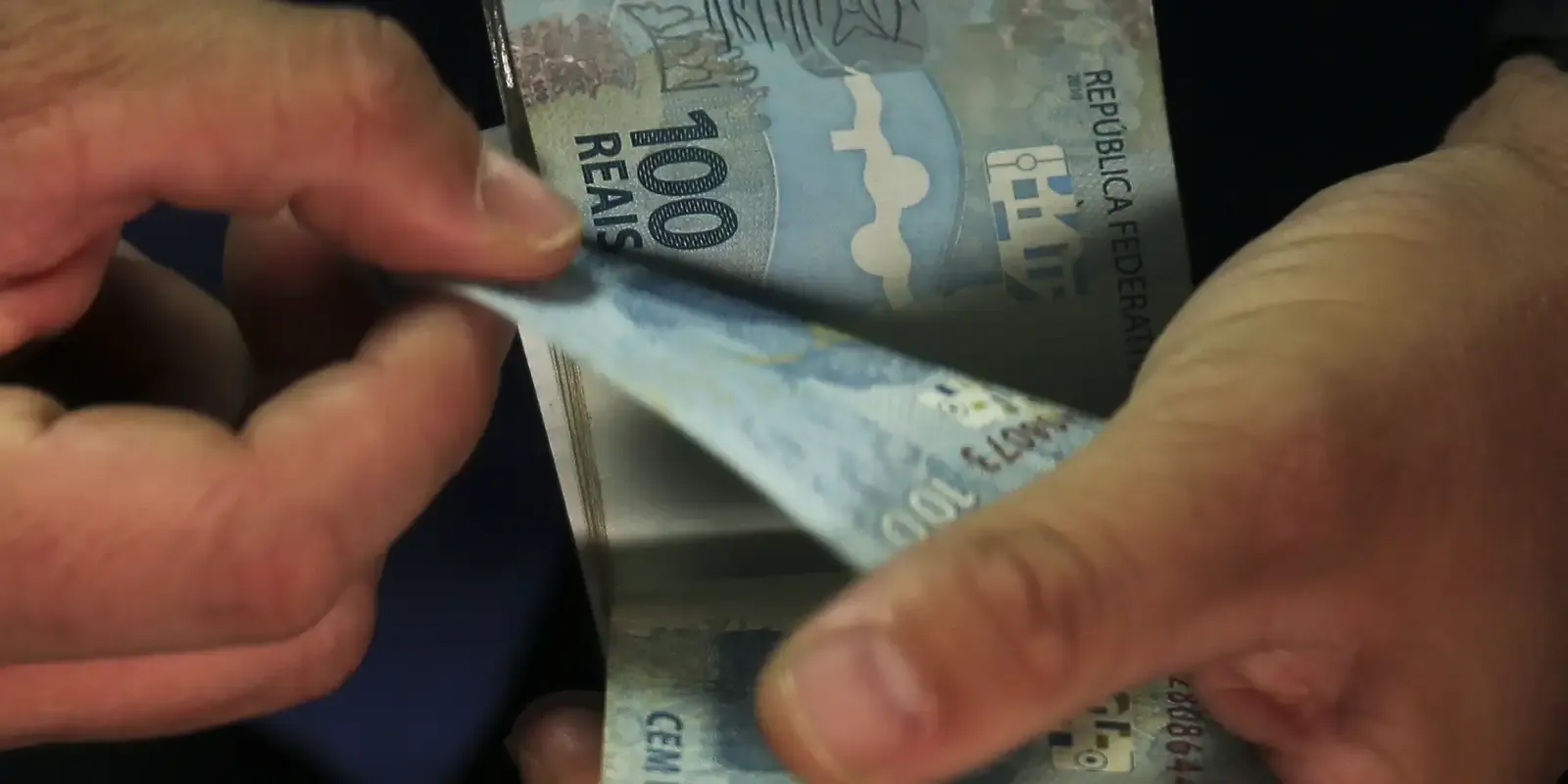 Contagem de notas de 100 reais Mãos masculinas manuseando notas de 100 reais.