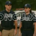 Dois agentes da Guarda Municipal uniformizados ao lado de viatura durante concurso público.