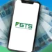 Aplicativo do FGTS exibido no celular com cédulas de 100 reais ao fundo