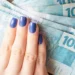 Notas de 100 reais sendo seguradas por uma mão com unhas pintadas