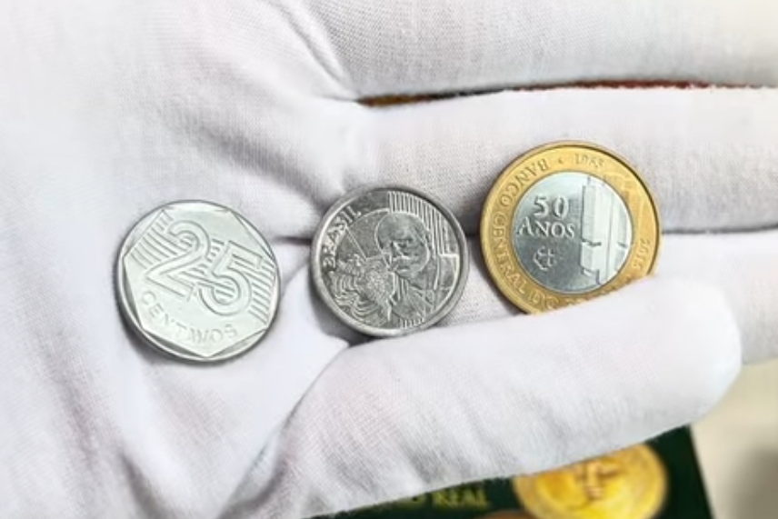 Três moedas brasileiras raras sendo exibidas por colecionador com luva branca