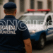Vista traseira de um Guarda Municipal uniformizado com o texto "GUARDA MUNICIPAL" no colete, olhando para uma viatura policial com luzes de emergência. A palavra "CONCURSO" está em destaque sobre a imagem.