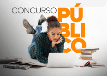 Jovem estudando para concurso público no notebook, rodeada de livros abertos no chão.
