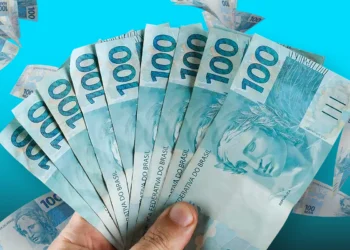 Notas de 100 reais em mãos, simbolizando indícios de riqueza ou compensações financeiras.