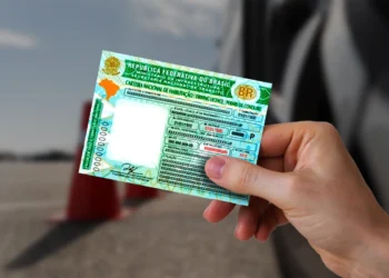 Carteira Nacional de Habilitação (CNH) do Brasil sendo segurada por uma pessoa, com fundo desfocado de cones de sinalização, ilustrando o tema sobre as vagas para CNH gratuita.