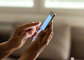 Mãos segurando smartphone enquanto navegam na tela em ambiente interno.