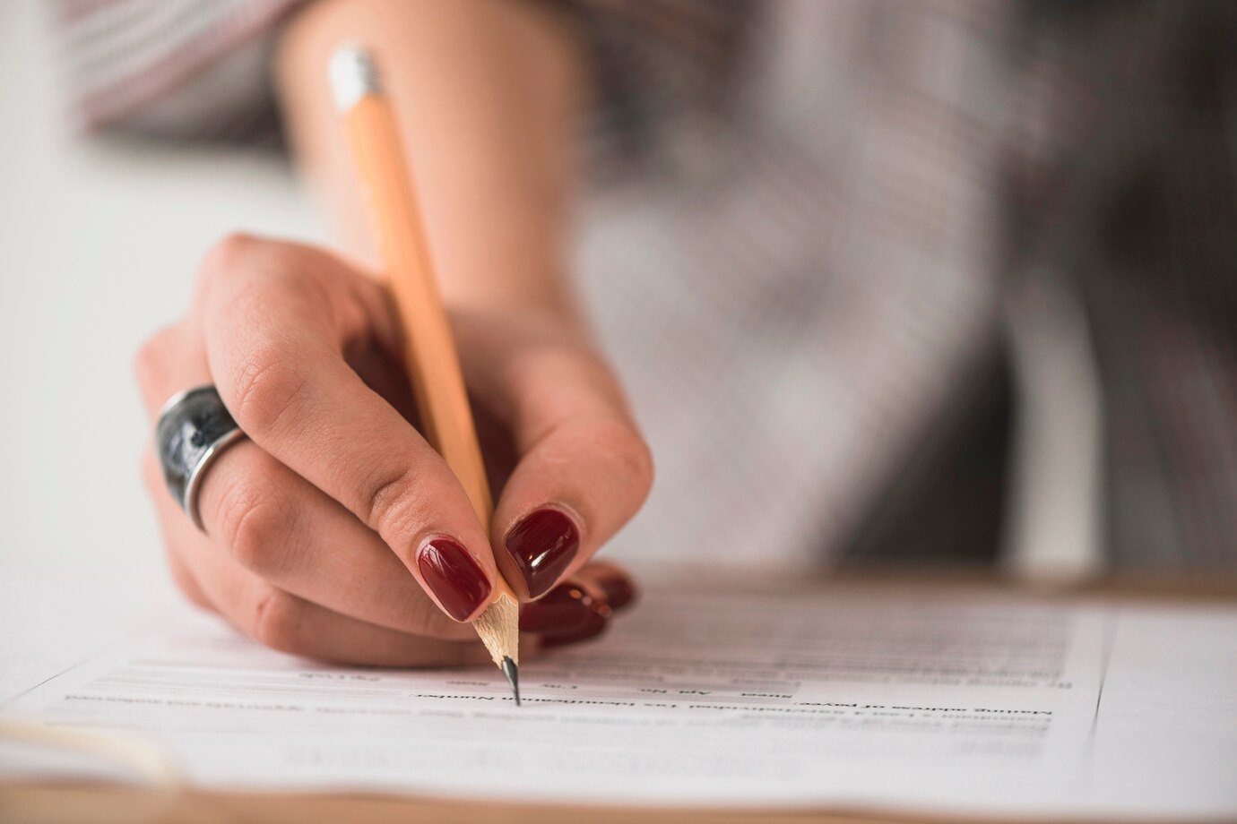 concurso da Prefeitura Mão feminina preenchendo formulário com lápis grafite em folha de papel.