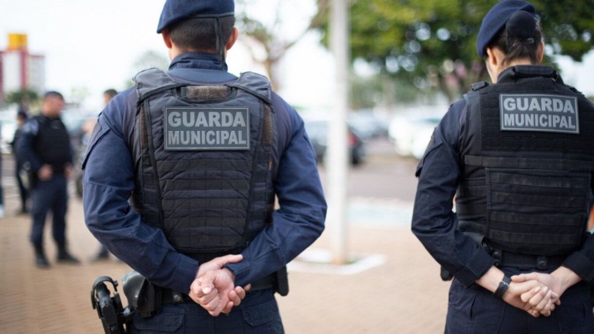 Guardas municipais de costas durante patrulhamento em área urbana.