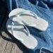 Um par de sandálias Havaianas brancas, modelo Slim, sobre uma calça jeans em uma superfície de madeira.