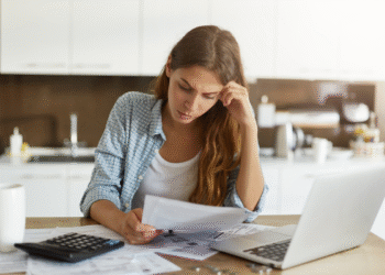 Mulher preocupada analisando contas e usando calculadora na cozinha.