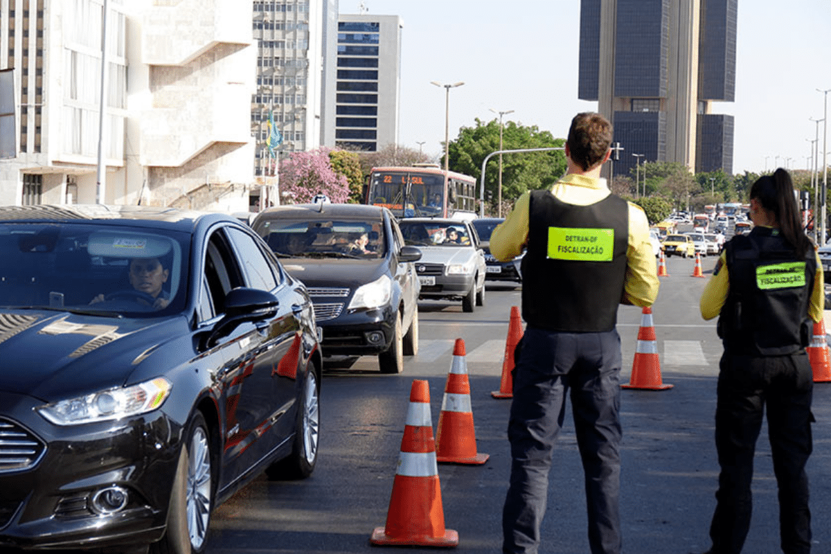 Agentes do Detran realizam fiscalização em avenida com carros e cones.