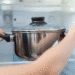 Pessoa colocando uma panela de inox com tampa na geladeira aberta.