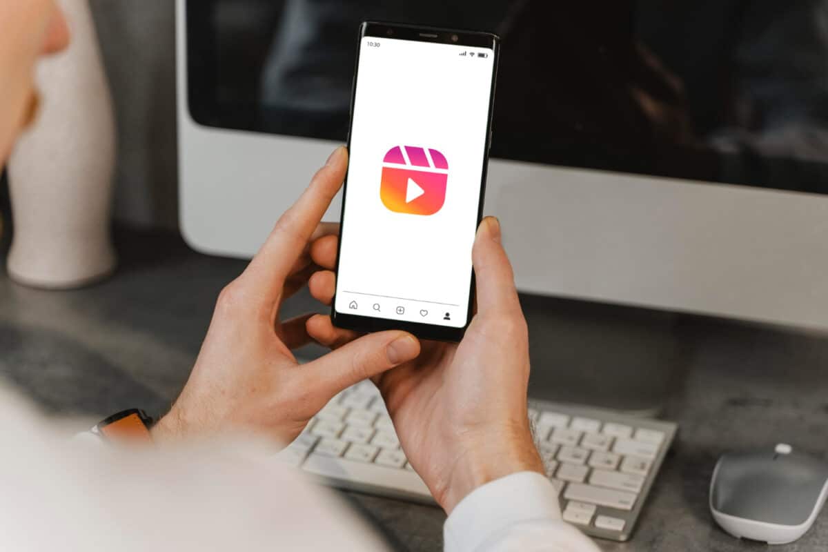 Pessoa segurando smartphone com aplicativo Instagram Reels aberto em ambiente de trabalho