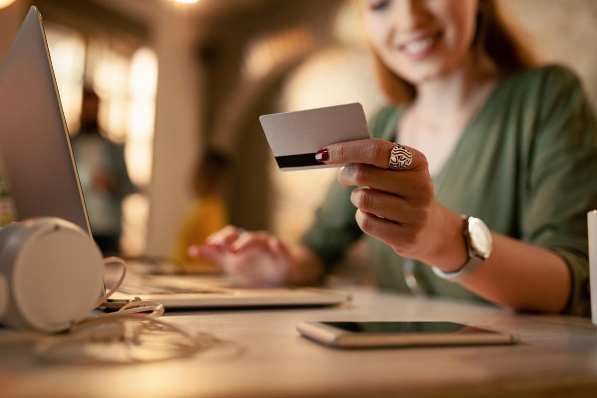 Mulher segurando cartão de crédito fazendo compra online em notebook com celular na mesa