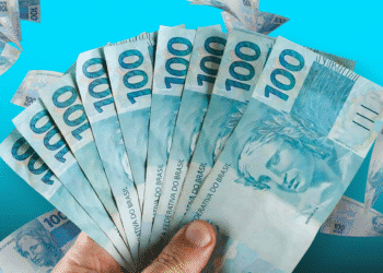 Imagem de mãos segurando várias notas de 100 reais com fundo azul, relacionada ao tema "Quem tem direito à primeira parcela do 13º salário?"