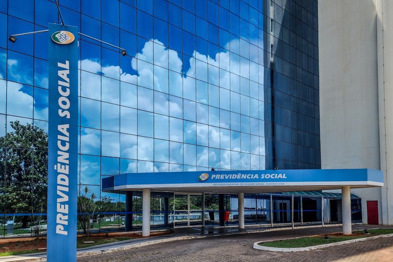 Fachada do prédio da Previdência Social refletindo o céu, representando o atendimento aos beneficiários do INSS no Brasil.