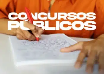 Pessoa escrevendo em caderno com caneta vermelha, focada em estudo para concursos públicos.