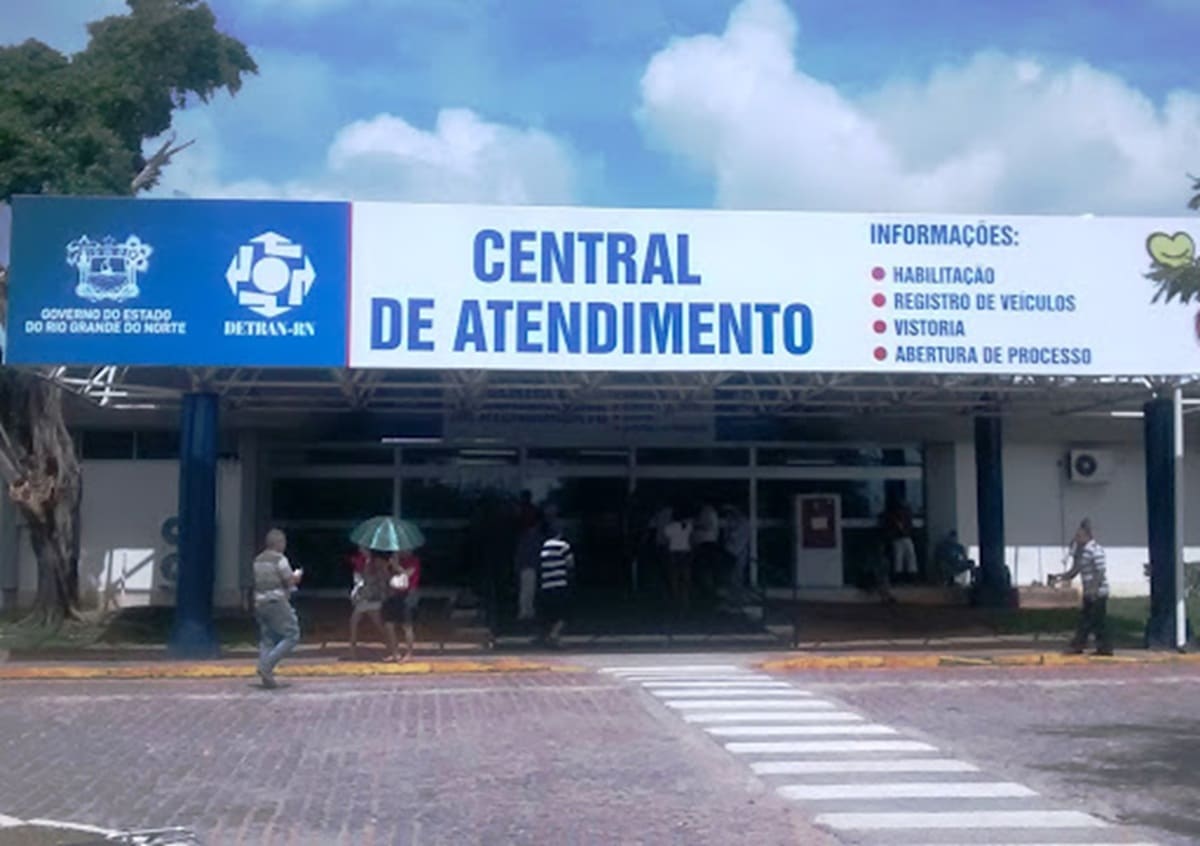 Fachada da Central de Atendimento Detran-RN com cidadãos circulando e serviços de habilitação e veículos listados