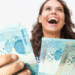 Mulher sorridente segurando notas de 100 reais comemorando aumento salarial
