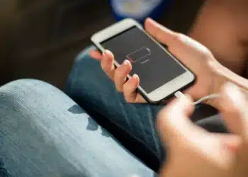 Pessoa carregando celular com bateria baixa, mostrando o ícone de carregamento no dispositivo.