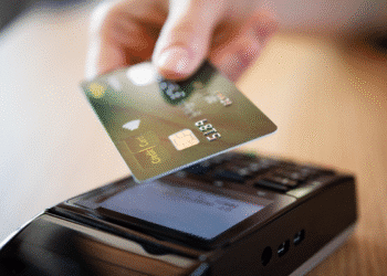 Mão segurando cartão de crédito próximo à maquininha para pagamento por aproximação