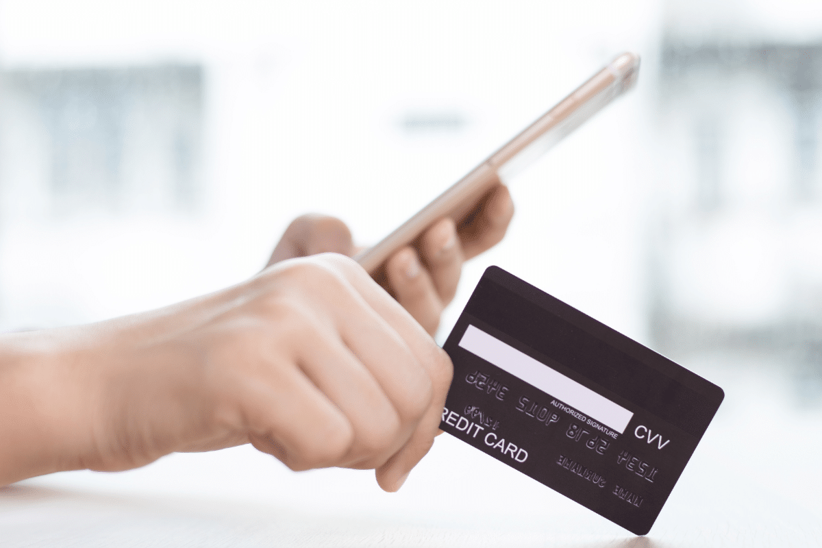 Mão segurando cartão de crédito e celular para pagamento online seguro