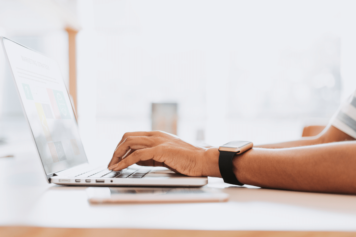 Mão de pessoa usando smartwatch digitando em laptop em ambiente claro e limpo