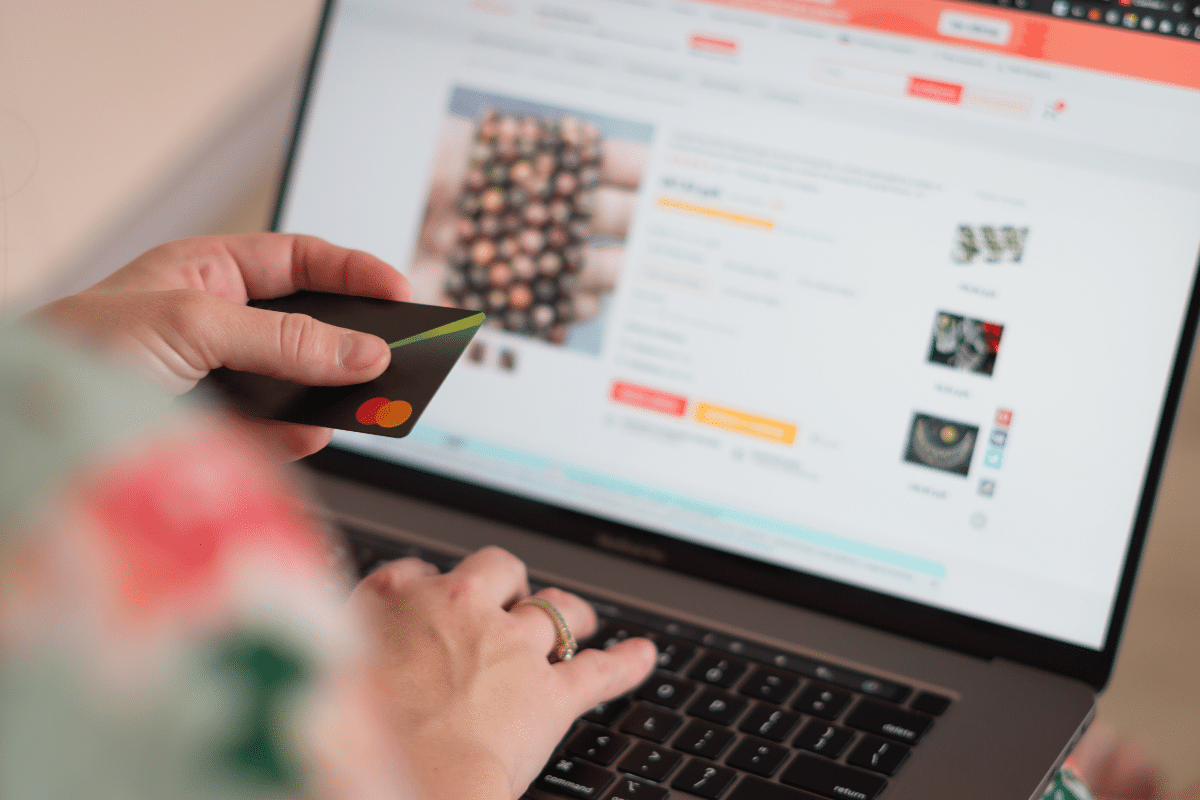 Mãos segurando cartão de crédito preto enquanto faz compra em laptop
