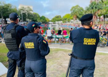 Três agentes da Guarda Civil Municipal vigiam evento ao ar livre com público numeroso em área gramada