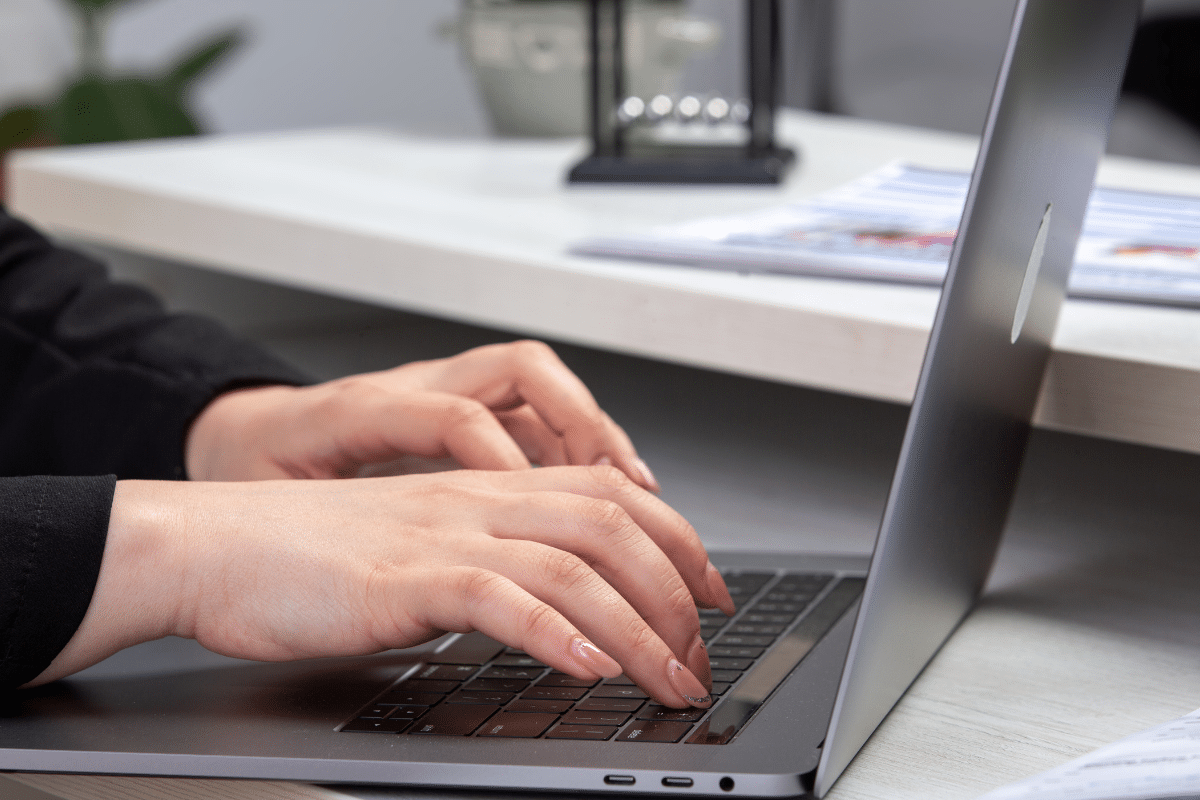 Mãos femininas digitando em notebook cinza em ambiente de trabalho