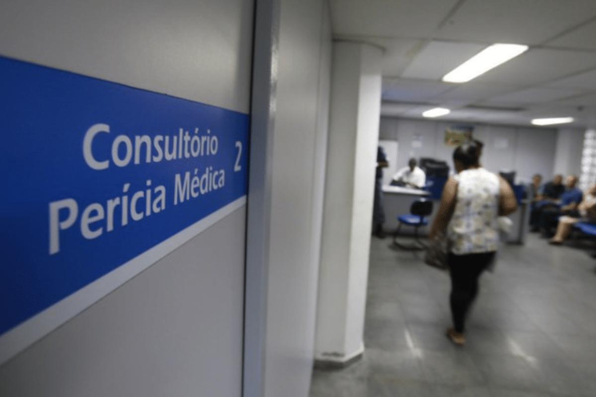 Entrada de consultório de perícia médica com placa azul e pessoas aguardando atendimento em sala de espera