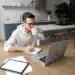 Homem trabalhando de casa com laptop e caderno, refletindo as profissões remotas em alta no mercado.
