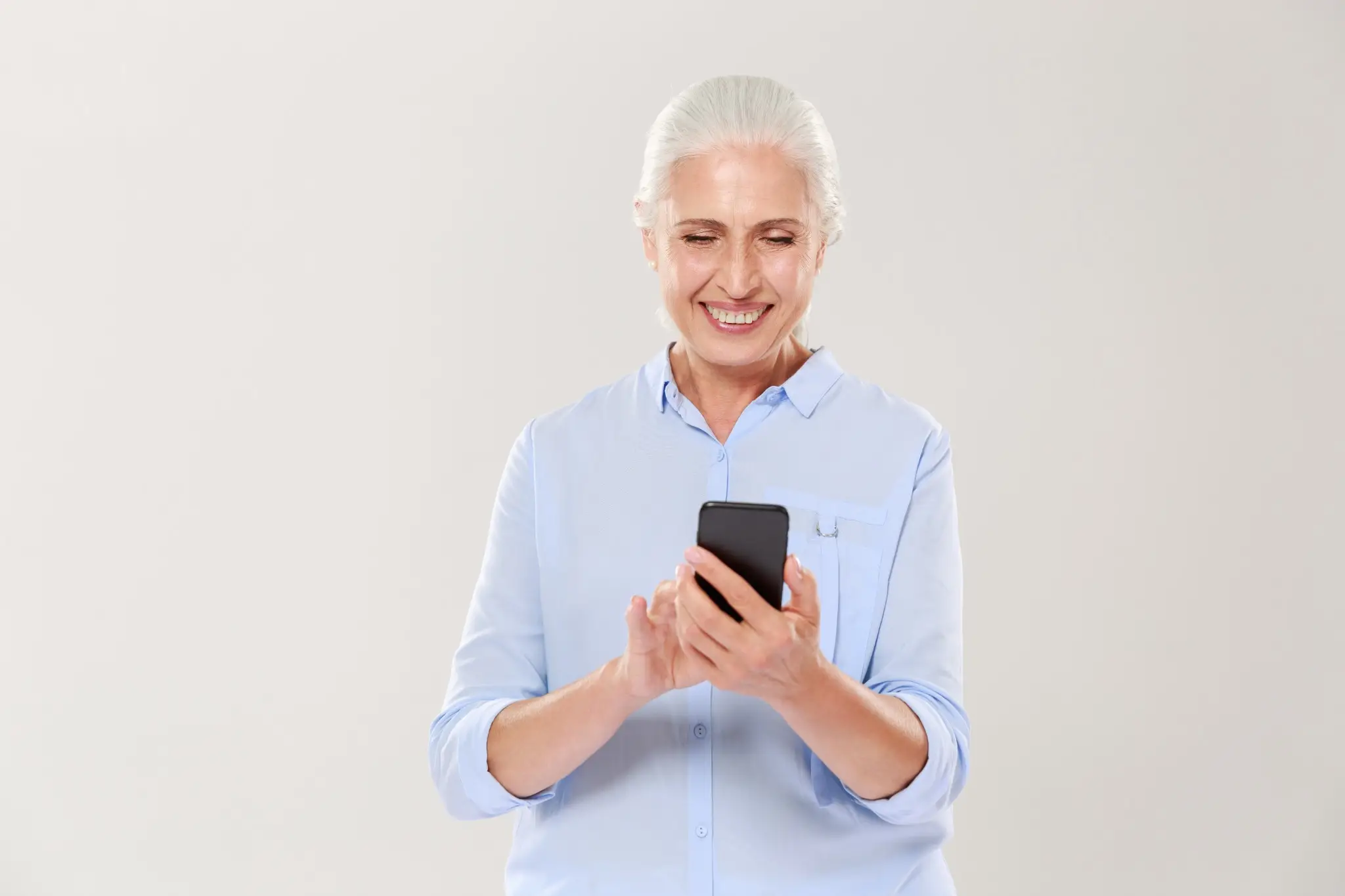 Mulher sorridente usando smartphone para realizar a prova de vida de forma digital, isolada em fundo claro.