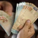 Dinheiro em notas de 50 reais sendo segurado, simbolizando o Saque-Aniversário do FGTS ou empréstimo consignado CLT.
