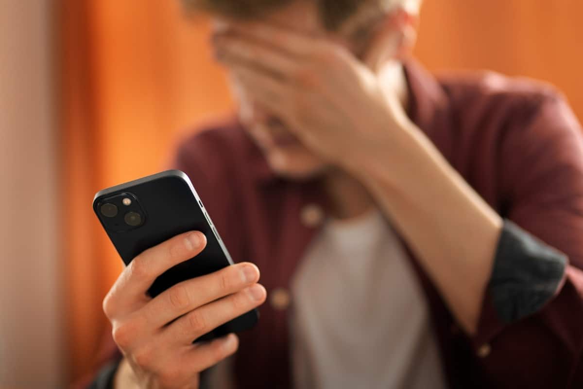 Pessoa preocupada com mão na cabeça olhando smartphone após identificar possíveis sinais de invasão no WhatsApp