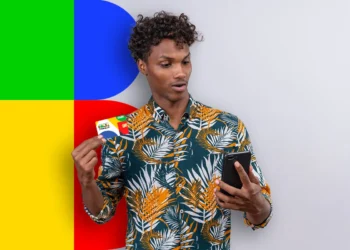 Homem olhando seu celular enquanto segura o cartão do Bolsa Família, com fundo colorido.