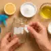 Pessoa removendo um rótulo de frasco de vidro com algodão e ingredientes naturais como limão, óleo e bicarbonato