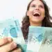 Mulher sorrindo enquanto segura notas de R$ 100, representando o benefício do Governo com a entrega de R$ 300.
