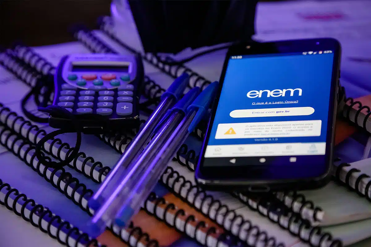 Materiais de estudo para o ENEM (celular com app do ENEM, calculadora, canetas e cadernos) em um ambiente com pouca luz, simbolizando a dedicação e o planejamento do cronograma de estudos para a reta final de 2025.