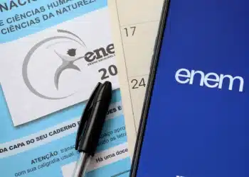 Caneta preta sobre caderno do ENEM e celular com logo do ENEM na tela azul