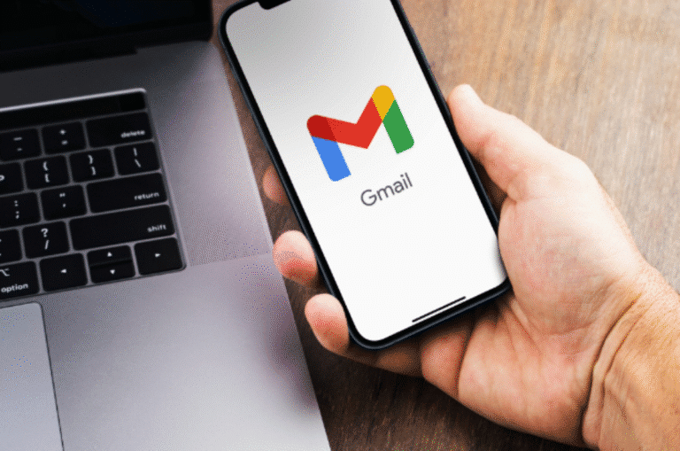 Pessoa segurando celular com o aplicativo Gmail aberto ao lado de um notebook