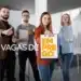 Grupo de profissionais felizes mostrando sinal de positivo, com uma pessoa segurando um quadro com a palavra 'VAGAS DE EMPREGO', referindo-se a novas oportunidades de trabalho abertas.