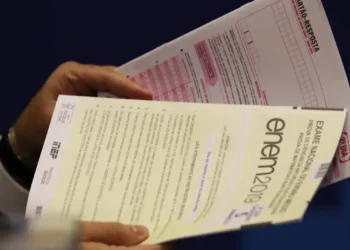Mãos segurando prova do ENEM 2019 junto com cartão-resposta para exame nacional do ensino médio