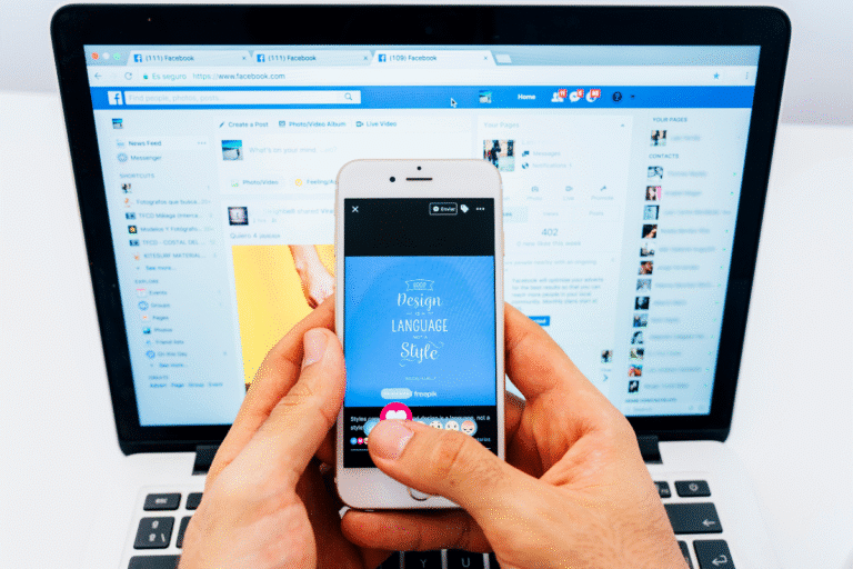 Pessoa segurando smartphone mostrando postagem no Facebook com laptop ao fundo exibindo a rede social.