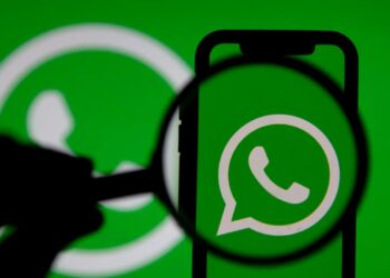 Ícone do WhatsApp ampliado sob uma lupa em fundo verde.