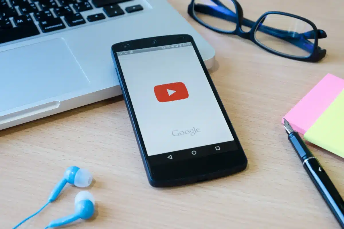 Celular com app do YouTube aberto mostrando a interface inicial, com o ícone do YouTube destacado.