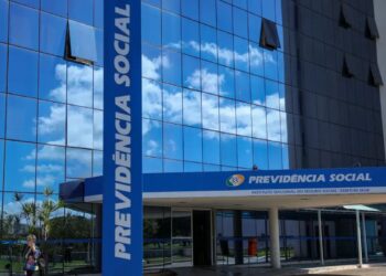 Fachada de vidro moderna e azul da sede do INSS (Instituto Nacional do Seguro Social) sob céu parcialmente nublado.